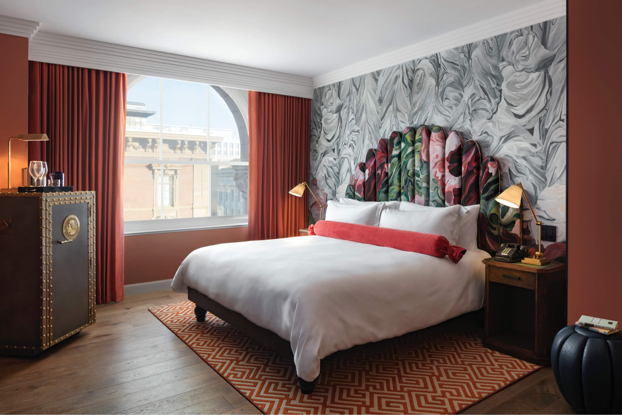 Stylish hotel room with a bold floral headboard, marble-effect wallpaper, and large windows offering natural light.