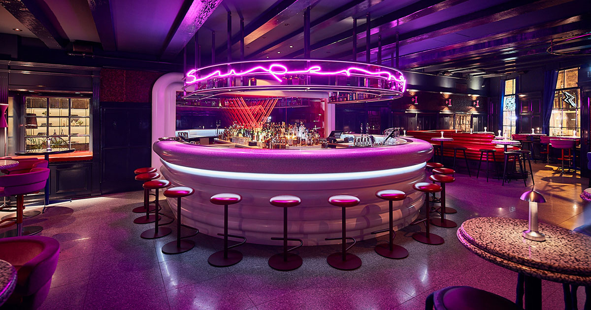 Vibrant, neon-lit bar at Super Lyan featuring a circular counter with modern stools and a futuristic ambiance.