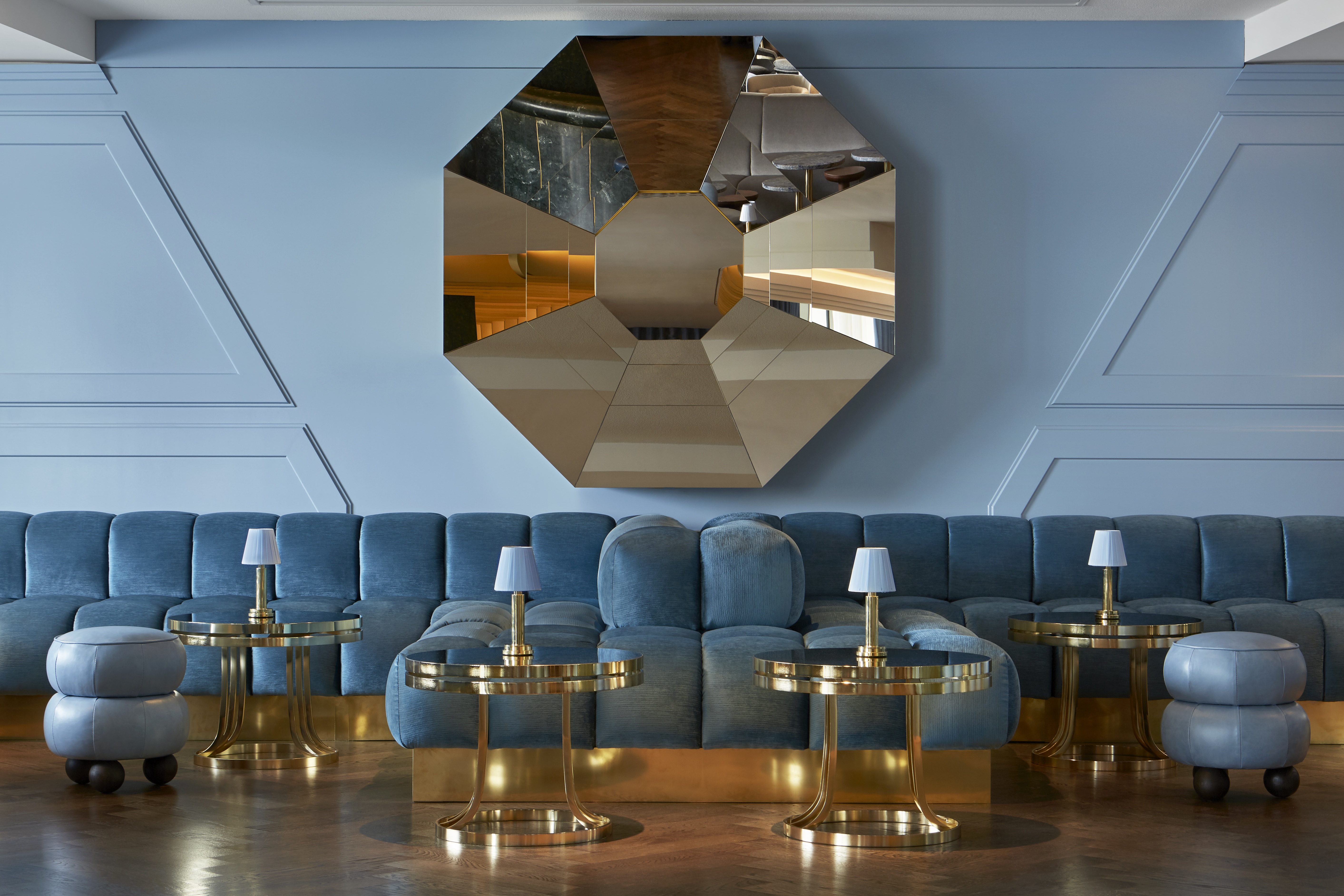Stylish lounge with blue velvet seating, gold accents, and a large geometric mirror, creating a luxurious atmosphere.