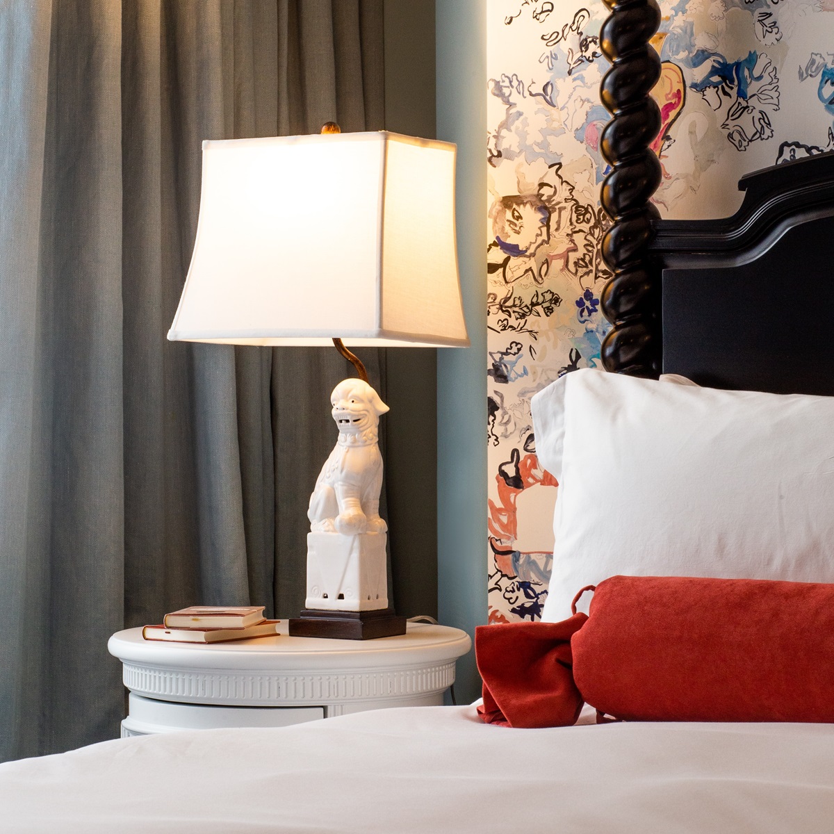 Close-up of a stylish hotel room corner with a modern lamp with a dog and wallpaper behind a large bed.