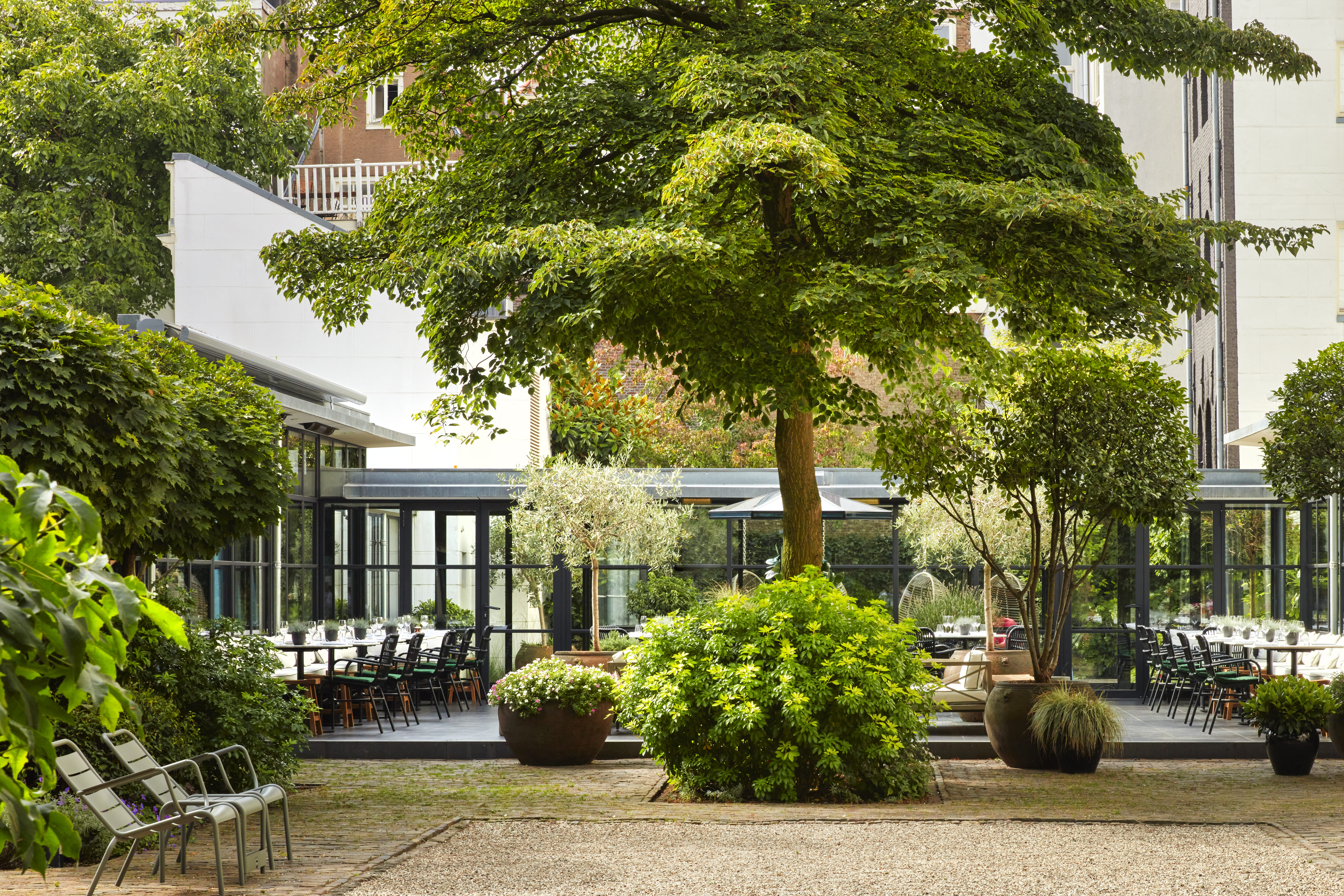 Lush garden courtyard at Pulitzer Garden i Amsterdam with outdoor dining tables and glass-walled building.