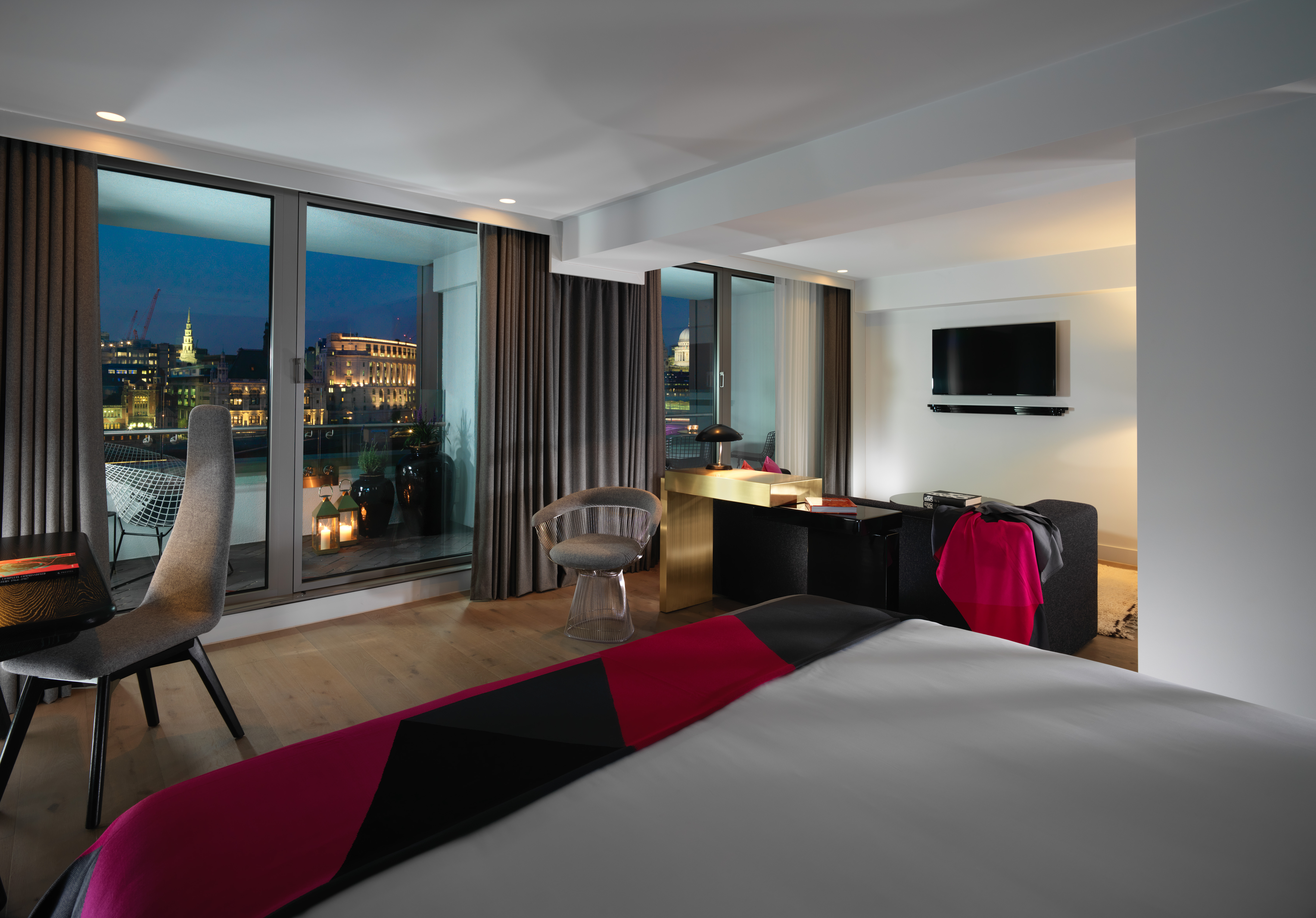 A luxurious hotel suite with a balcony offering a stunning river view, featuring modern decor.