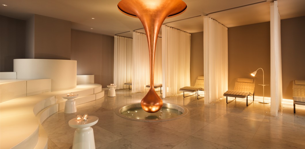Serene relaxation room at Agua Spa with modern, minimalist design, featuring a large copper water feature centerpiece.