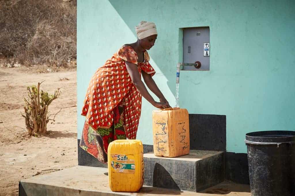 Woman is filling up tanks with fresh water by a building.