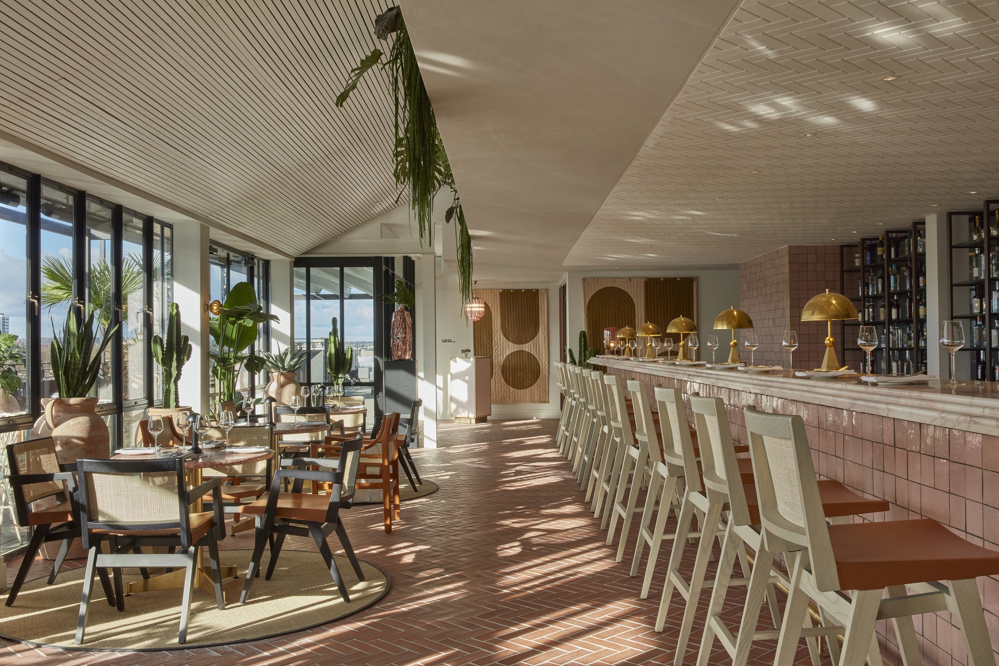Stylish restaurant and bar area in OHS London with ample light, cacti, light pink colours and wooden furniture.