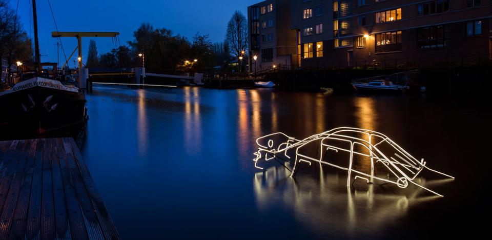 Nighttime view of a light installation over water, depicting a glowing, abstract outline of a vehicle.