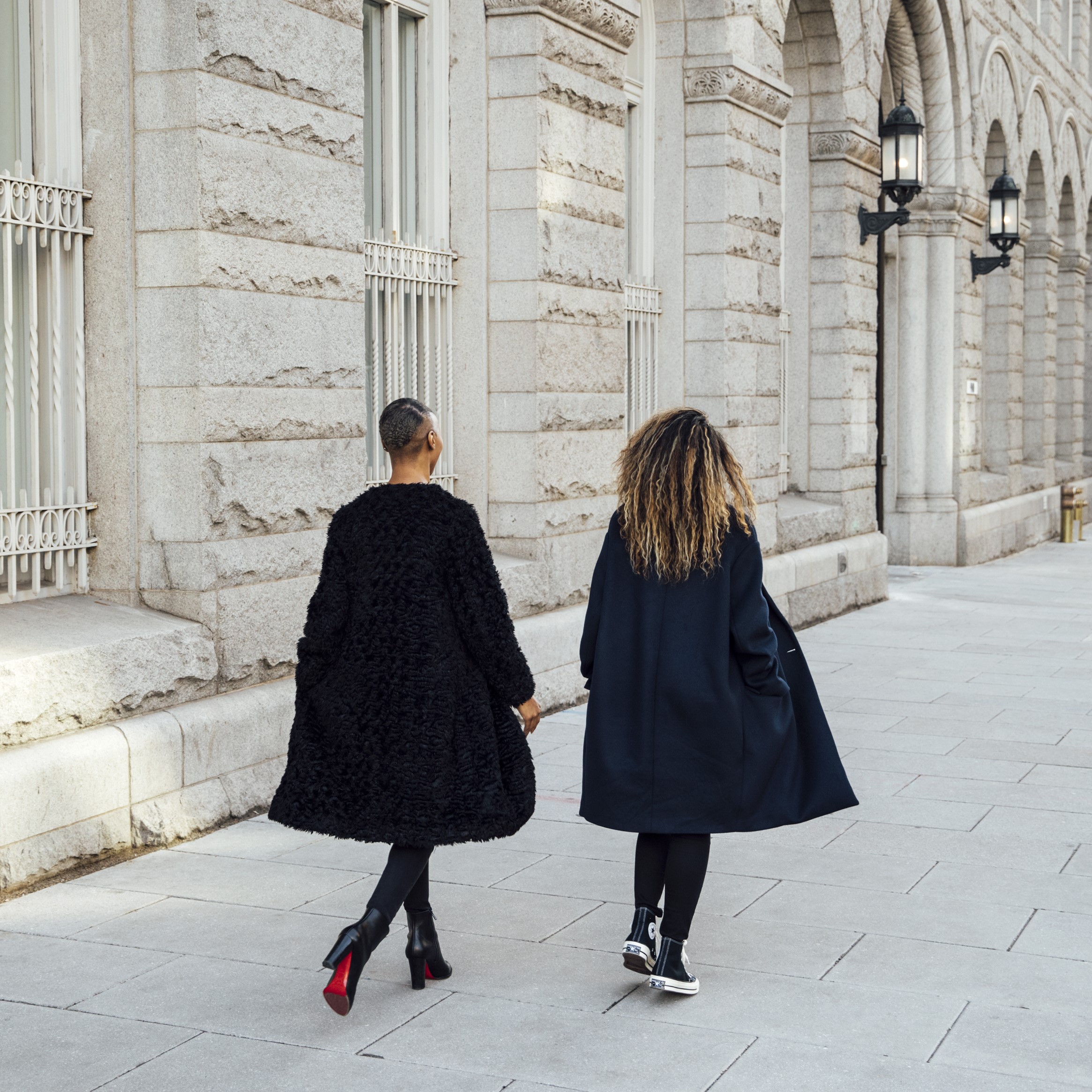 Two well-dressed women walking in the street next to a beautiful traditional building.