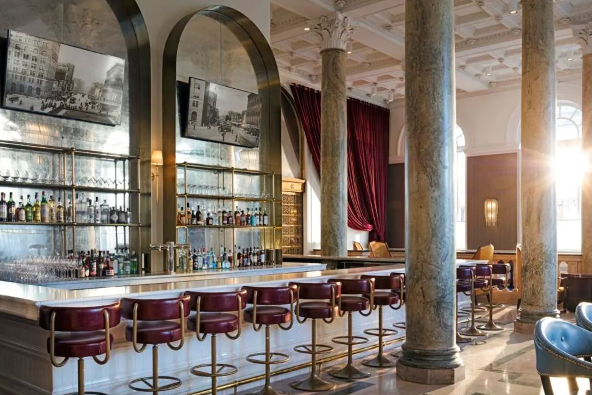 Luxurious interior of the bar area at the Riggs DC hotel with marble columns and red leather bar stools.