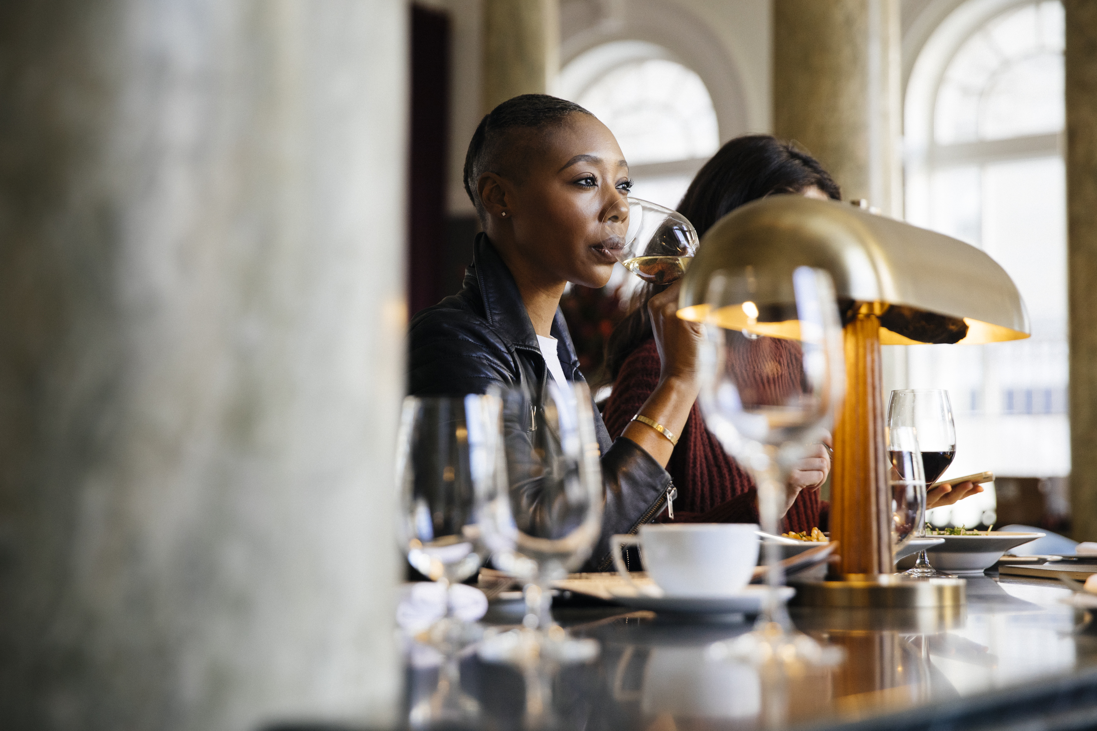 Chic interior at Cafe Riggs with a woman sipping white wine in a modern setting with stylish design and marble columns.
