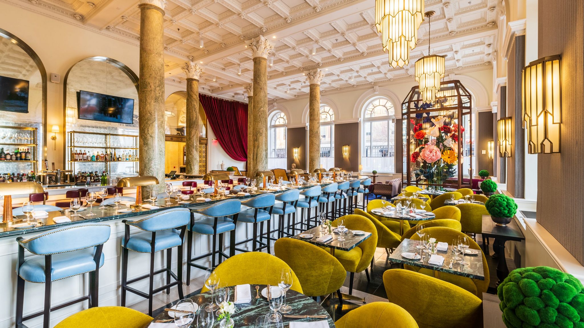 Stylish hotel room with a bold floral headboard, marble-effect wallpaper, and large windows offering natural light.