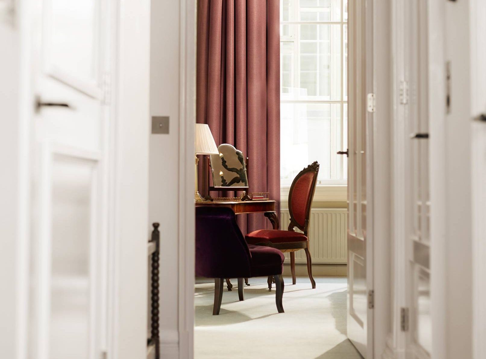 Luxurious hotel room with velvet chairs, a writing desk, and rich, warm curtains, offering a sophisticated ambiance.