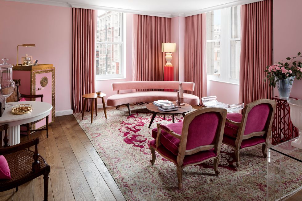 Luxurious hotel suite featuring elegant pink decor, with velvet chairs, draped curtains, and a vintage-style rug.