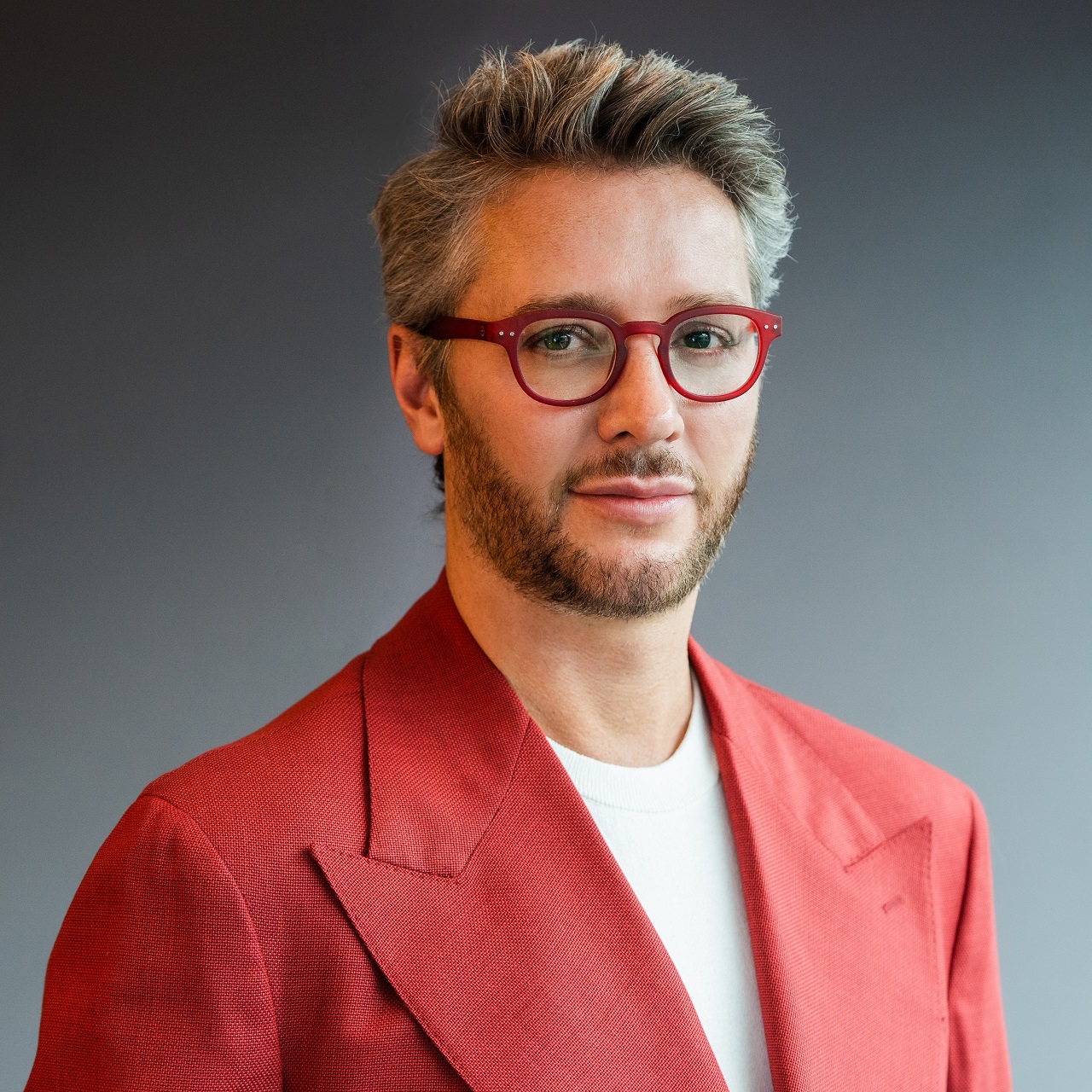 Professional shot of Lore Group designer Jacu Strauss in a stylish red suit with red glasses.