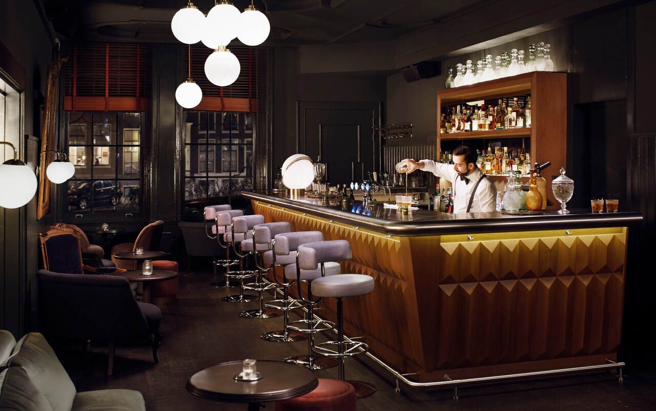 Pulitzer Bar with a modern decor, featuring a variety of drinks and stylish seating with a bartender pouring cocktails.