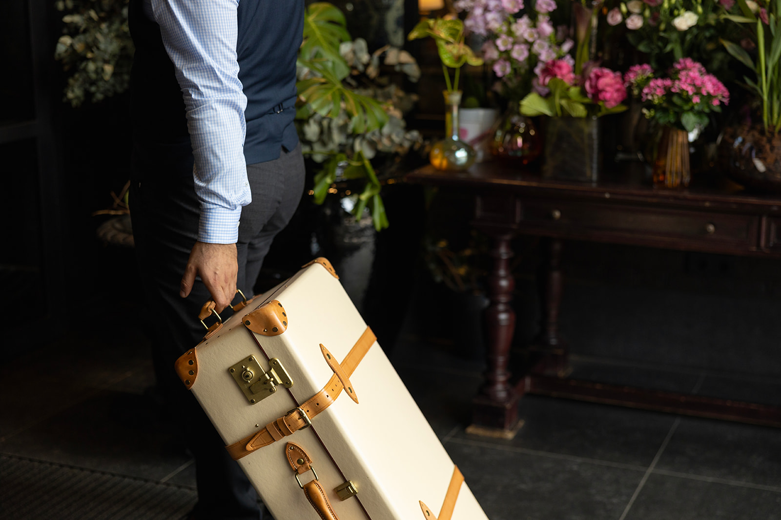 Person in vest and dress shirt holding a cream suitcase with tan leather straps promoting recruitment at Lore Group.
